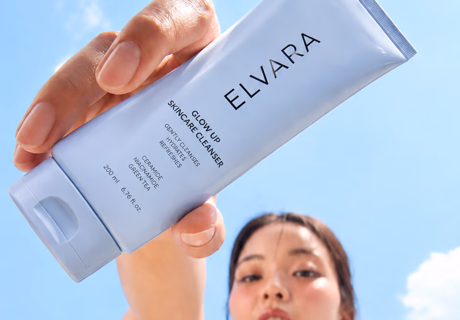 A woman holding the Elvara cleanser up against a blue sky